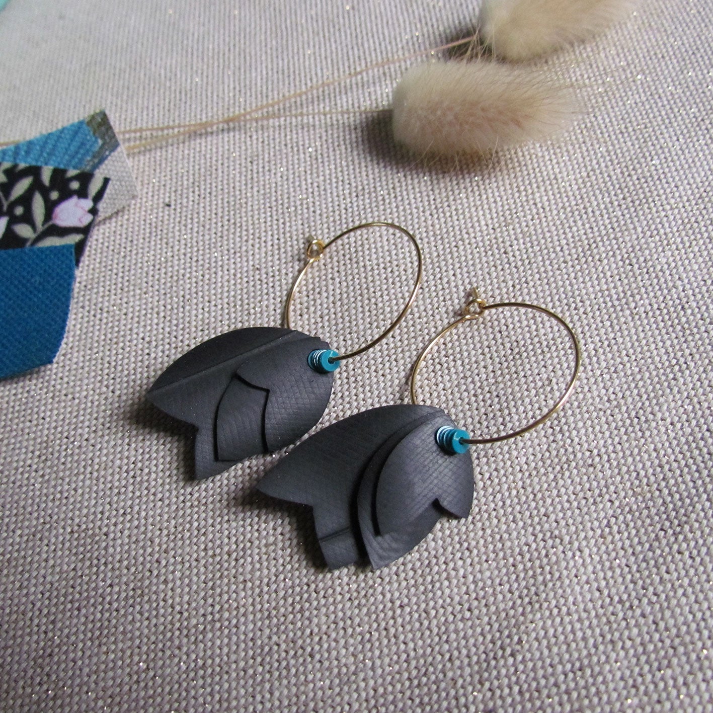 Boucles d'oreille créoles légères dorée aux pétales noires avec un soupçon de turquoise